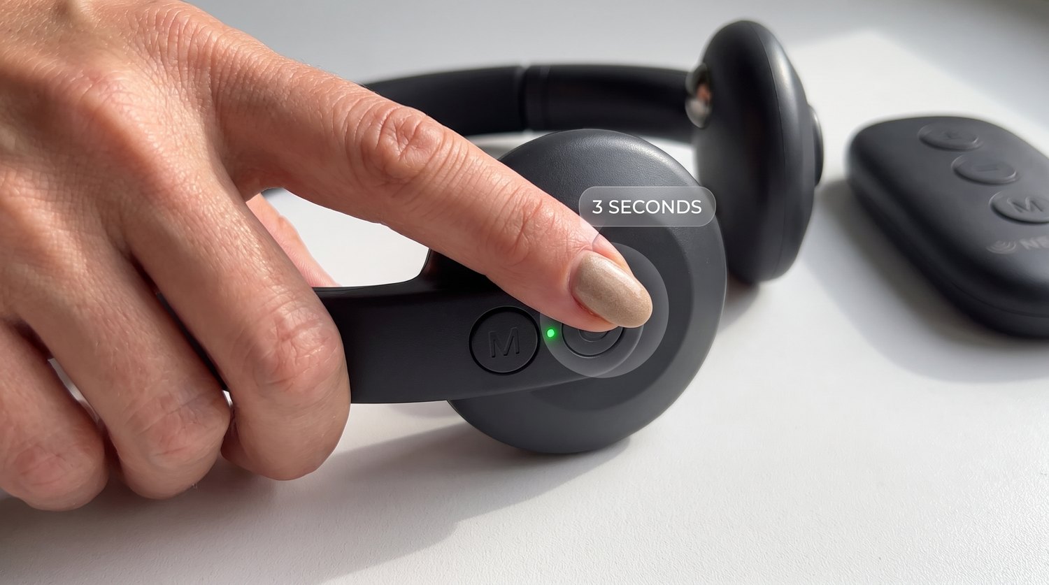 A finger pressing and holding the power button on the Nervelo device for 3 seconds, with the green light on